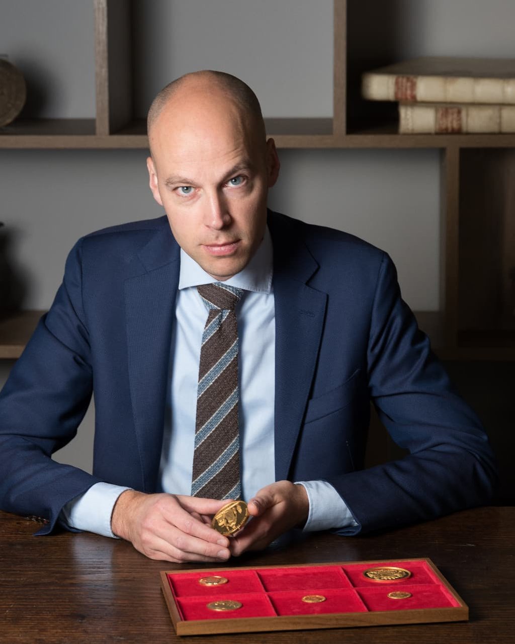 Hans Jongeling holding a gold coin at his desk, with a tray of further gold coins before him
